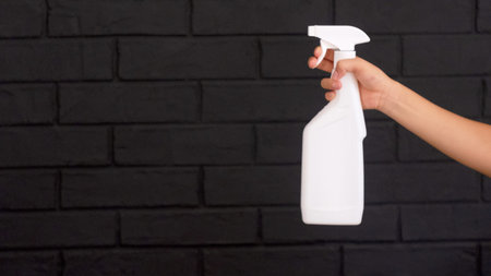 house cleaning, woman's hand with spray gun on black brick wall background