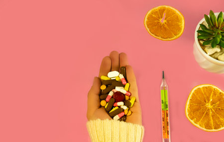 multicolored pills in hand on a pink background, thermometer on the table, dried oranges, indoor flower, home succulent, top view copy space for banner.の写真素材
