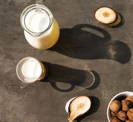 Glass jug and a glass of milk on the table with hard trend shadows, gray textured background, wood...