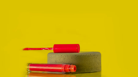 Liquid lipstick and applicator on a yellow colored background. An open tube of lip gloss and a brush...