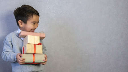 Ideal gifts for children. Happy child holds gifts in his hands. Looking away. Handsome boy wearing a white shirt and gray sweater. Happy Holidaysの写真素材