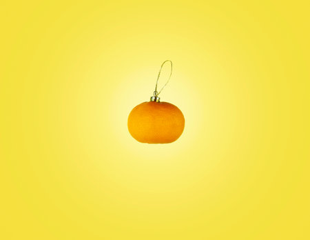 Banner with tangerine in the form of a Christmas tree toy on a yellow background. Merry Christmas or Happy New Year, yellow background with space for design and textの写真素材
