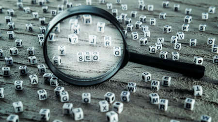 Magnifying glass search, letter cubes are scattered on the gray table and the word SEO highlighted with a magnifying glassの写真素材