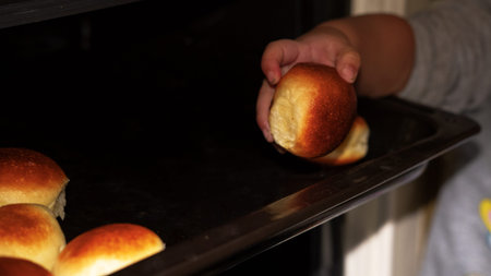 child's hand pulls out delicious rolls from the oven, home life, home lifestyle.
