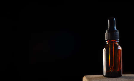 A glass dropper bottle with a pipette with a black rubber tip on a beautiful black background. The concept of nature skin. Organic Spa Cosmetics. A fashionable concept. The concept of a beauty salon and natural cosmetics.の写真素材