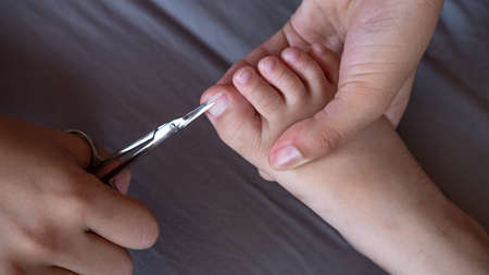 Closeup of female hands holding scissors to cut toe nails on tiny baby foot. Mom taking care of her child s hygieneの写真素材