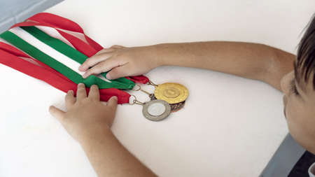 Concept of sporting success and victory smiling child champion athlete, child's hand holding medals for victory on the table.の写真素材