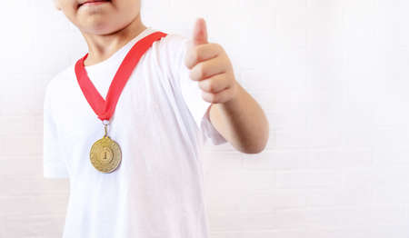 A happy teenage boy-dressed in a gold medal, smiles and gives a thumbs up to the camera, standing isolated against a white background. selective focus. the concept of sports and victoriesの写真素材