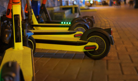 Electric scooters in a row at night in the parking lot. City bike rental system, public scooters on...