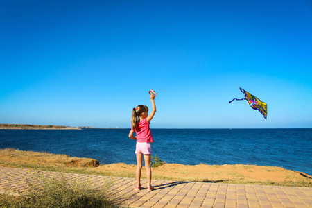 A little girl runs into the sky flying snake by the sea
