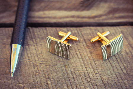 Pen and cufflinks on the old wood background. Toned image.の写真素材