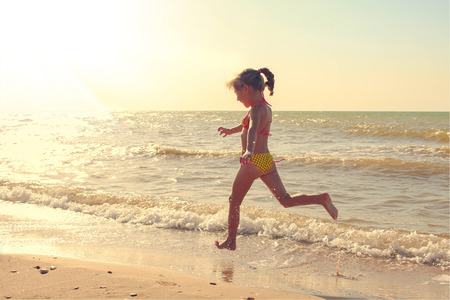 Girl in swimsuit runs along the shore of the sea. Toned imageの写真素材