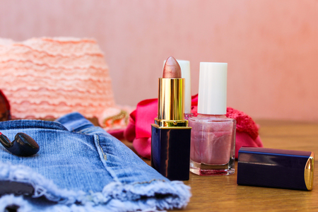 Cosmetics and women's accessories: lip gloss, nail polish, hat, denim shorts and headphones on tableの写真素材