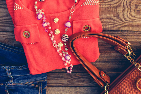 Women's clothing and accessories: sweater, jeans, handbag, beads on wooden background. Toned image.の写真素材
