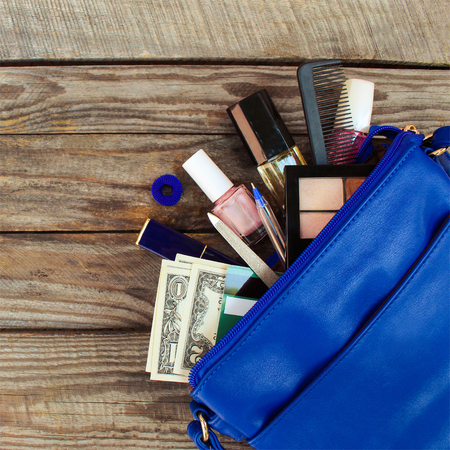Things from open lady handbag. women's purse on wood background. Cosmetics, money and women's accessories fell out of the blue handbag.の写真素材