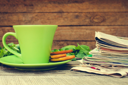 Cup of tea, mint, cookie, bunch of newspapers and magazines on wooden background. Toned image.の写真素材