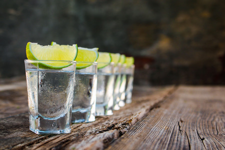 Vodka and lime slices on a wooden background.の写真素材