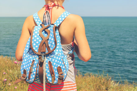 Girl with backpack looking at sea. Toned image.