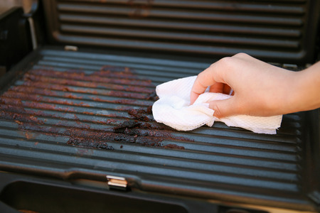 Dirty electric grill. Female hand wiping with cloth grill.の写真素材