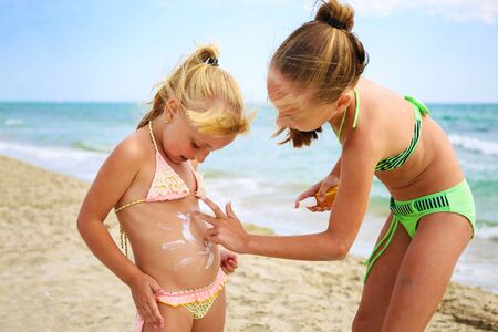 Sister applying protective sunscreen on young child. Girl draws sun cream on her stomach.