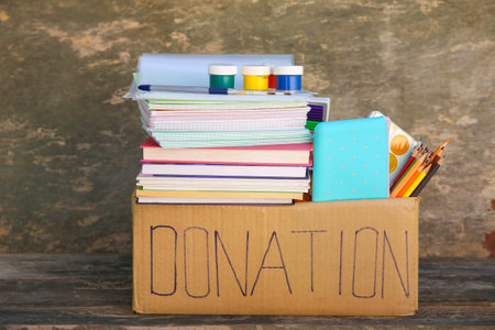 Donation box with school supplies on old wooden background.