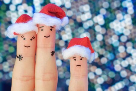 Fingers art of happy couple laughing in New Year hats. Man and woman hugs. Child is angry. Fingers art of couple celebrates Christmas. Toned image.の写真素材