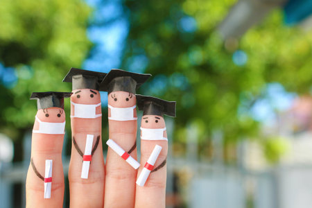 Fingers art of students in medical mask from COVID-2019. Graduates holding their diploma after...