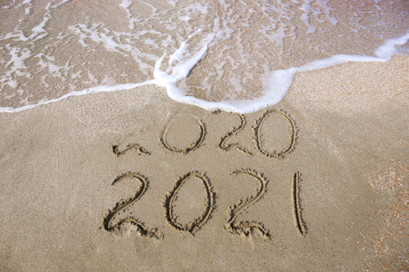 2020, 2021 years written on sandy beach sea. Wave washes away 2020.