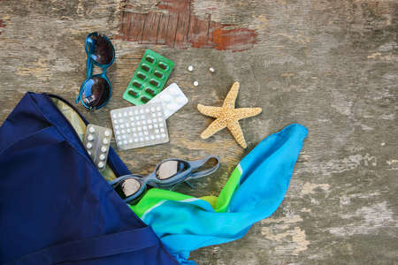 Summer women's beach accessories for your sea holiday and pill on old wooden background. Concept of medication required in journey. Top view.の写真素材
