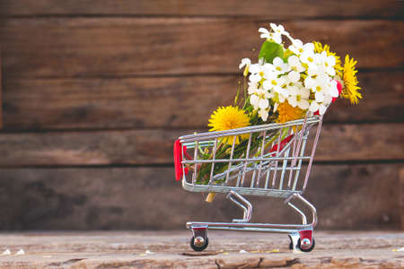 Shopping cart with flowers on the wooden background. toned image.の写真素材