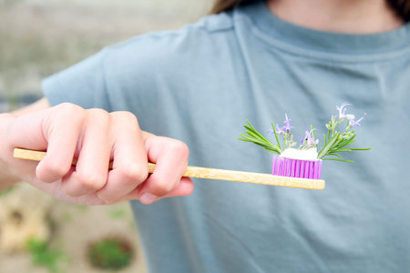 The girl holds a toothbrush with herbed toothpaste with rosemary in her hand. Selective focus on...