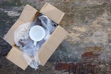 Packed cup in a plastic bubble wrap on an old wooden background. Fragile package.の写真素材