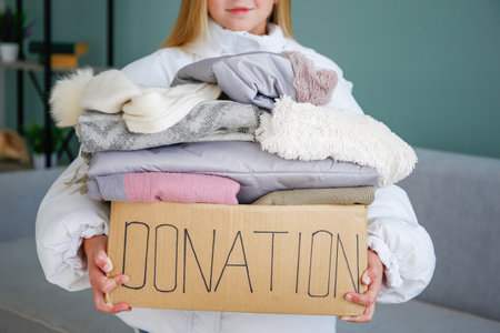 A child holds a donation box with clothes in the living room.の写真素材