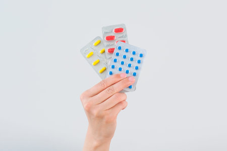 A woman's hand holds pills on a gray background.