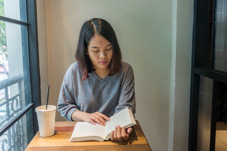 Asian Young woman in grey clothes reading book, drinking coffeeの写真素材