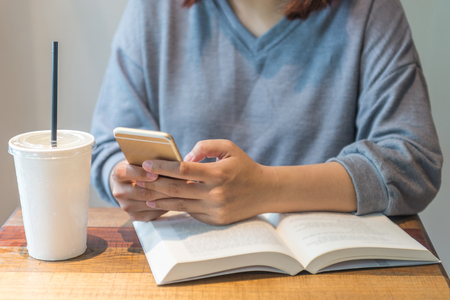 Woman hand texting message, reading book in the libraryの写真素材
