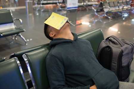 Man sleeping in the airport with book on faceの写真素材