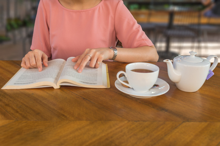 Woman hand drinking hot tea and reading booksの写真素材
