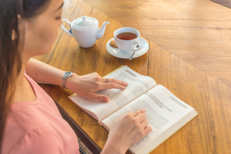Asian woman reading book and having a cup of tea