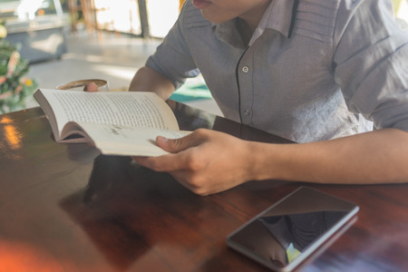 Human hand on the opened book with smartphone besideの写真素材