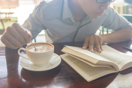 Young man reading book and stir coffee in the sunny day
