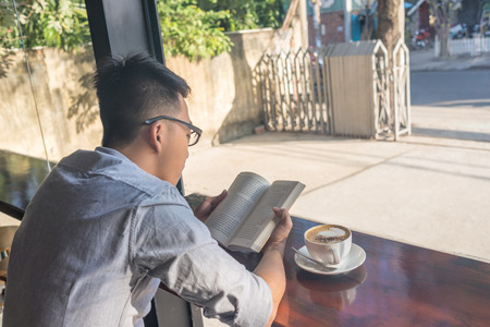 Young boy reading book with the cup of Cappuccino besideの写真素材