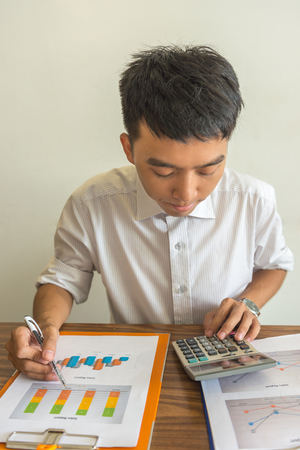 Vertical photo of business employee using calculator and reading financial reportの写真素材