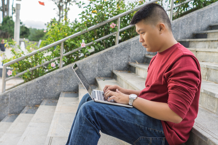 Side view of young Asian man working on laptop, sitting on stairの写真素材