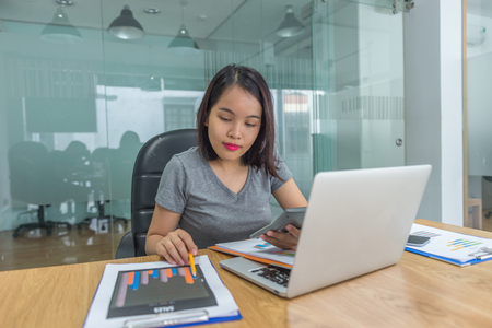 Young Asian manager wearing casual clothes, checking sales reports in her business office at weekendの写真素材