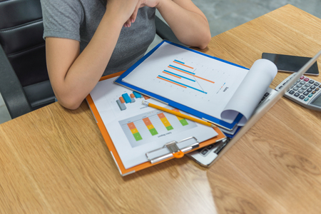 Businesswoman reading financial reports and working on laptop at workplaceの写真素材
