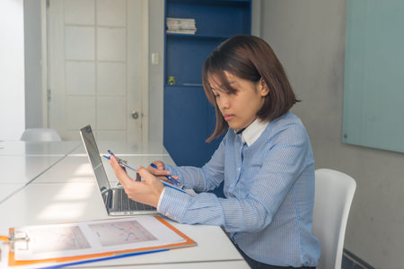 Young Asian businesswoman working on laptop with many financial reports on the table in the business...