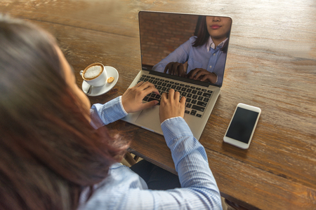 Young woman working on laptop with smartphone and hot cup of Cappuccino in the tableの写真素材