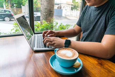 Side view of young man using laptop and drinking coffeeの写真素材