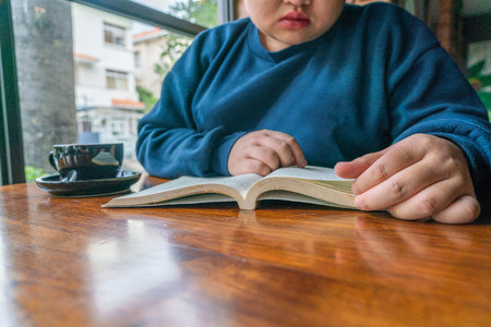 Young girl sitting by wooden table and reading bookの写真素材